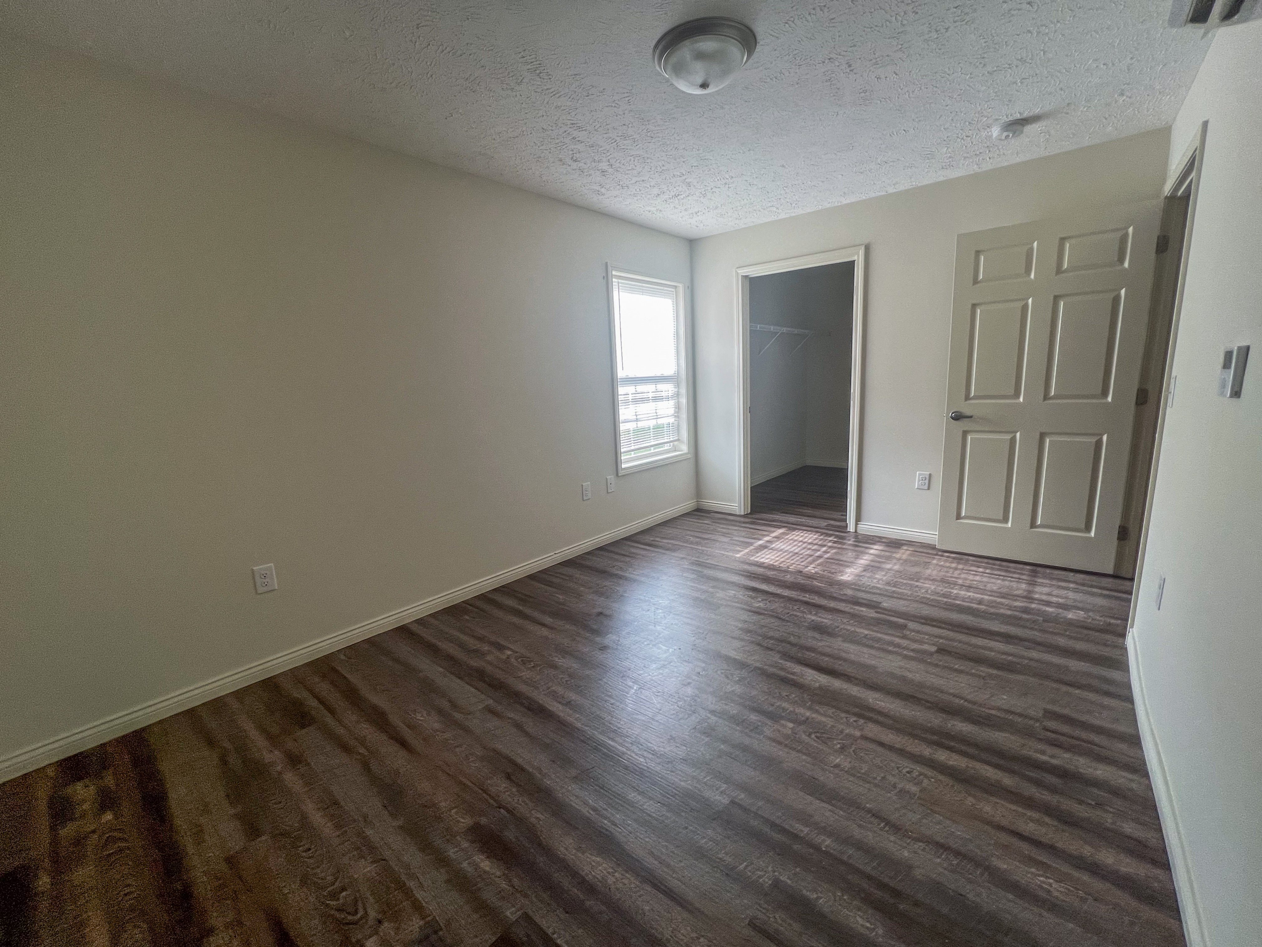 an empty living room with wooden floors and a door to a hallway